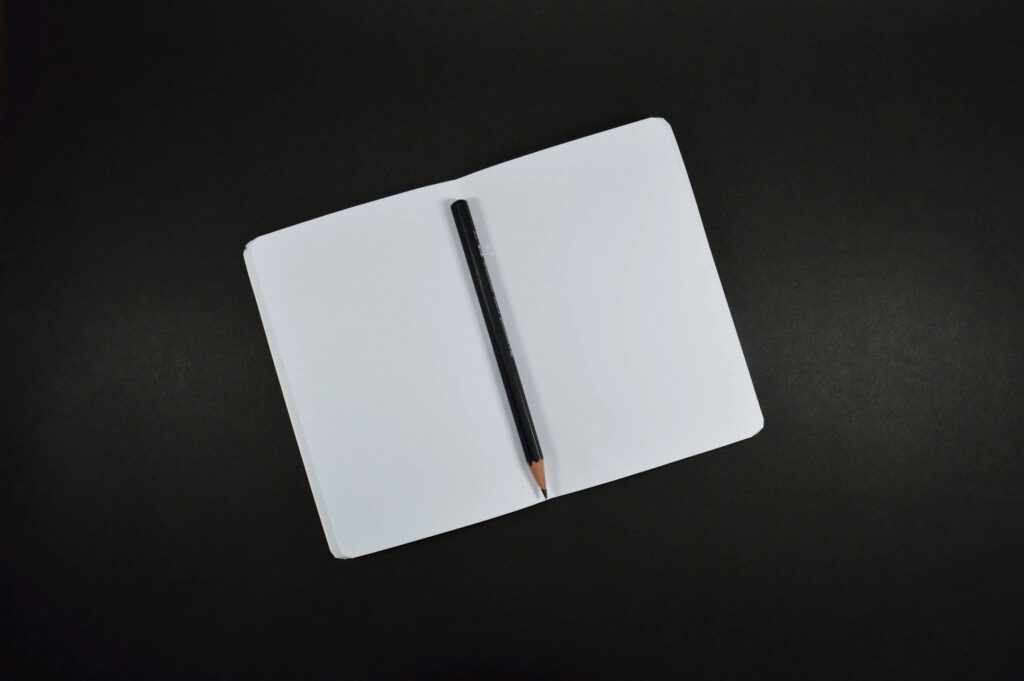a picture of a book on a black table with a pencil in the middle and empty pages